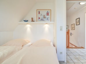 A bedroom with two beds, a ceiling light, a shelf with decorative items, and a staircase leading to another room. - Holiday Home With 1 Bedroom (Wrixum)