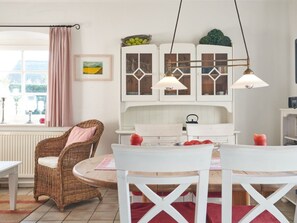 A cozy dining area with wicker chairs, a white table, and a cabinet with glass doors. - Holiday Home With 1 Bedroom (Wrixum)