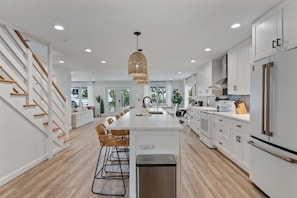 A modern kitchen with white cabinetry, a central island, and a stainless steel refrigerator. - Waves - Heated Pool -steps to Beach -golf Cart - Putting Green (Anna Maria)