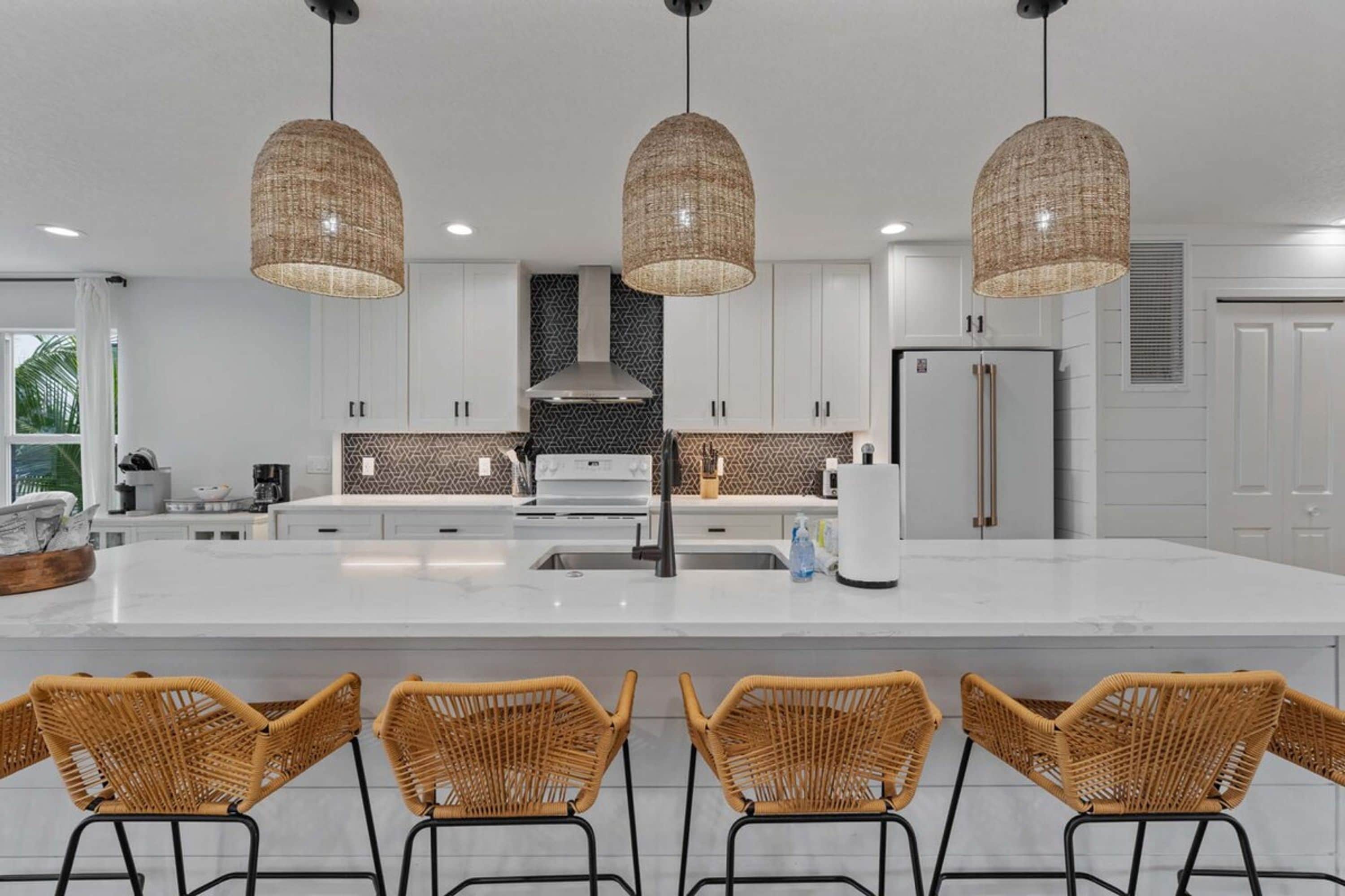 A modern kitchen with a large island, white cabinetry, and three wicker pendant lights.