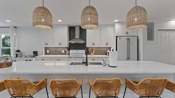 A modern kitchen with a large island, white cabinetry, and three wicker pendant lights.