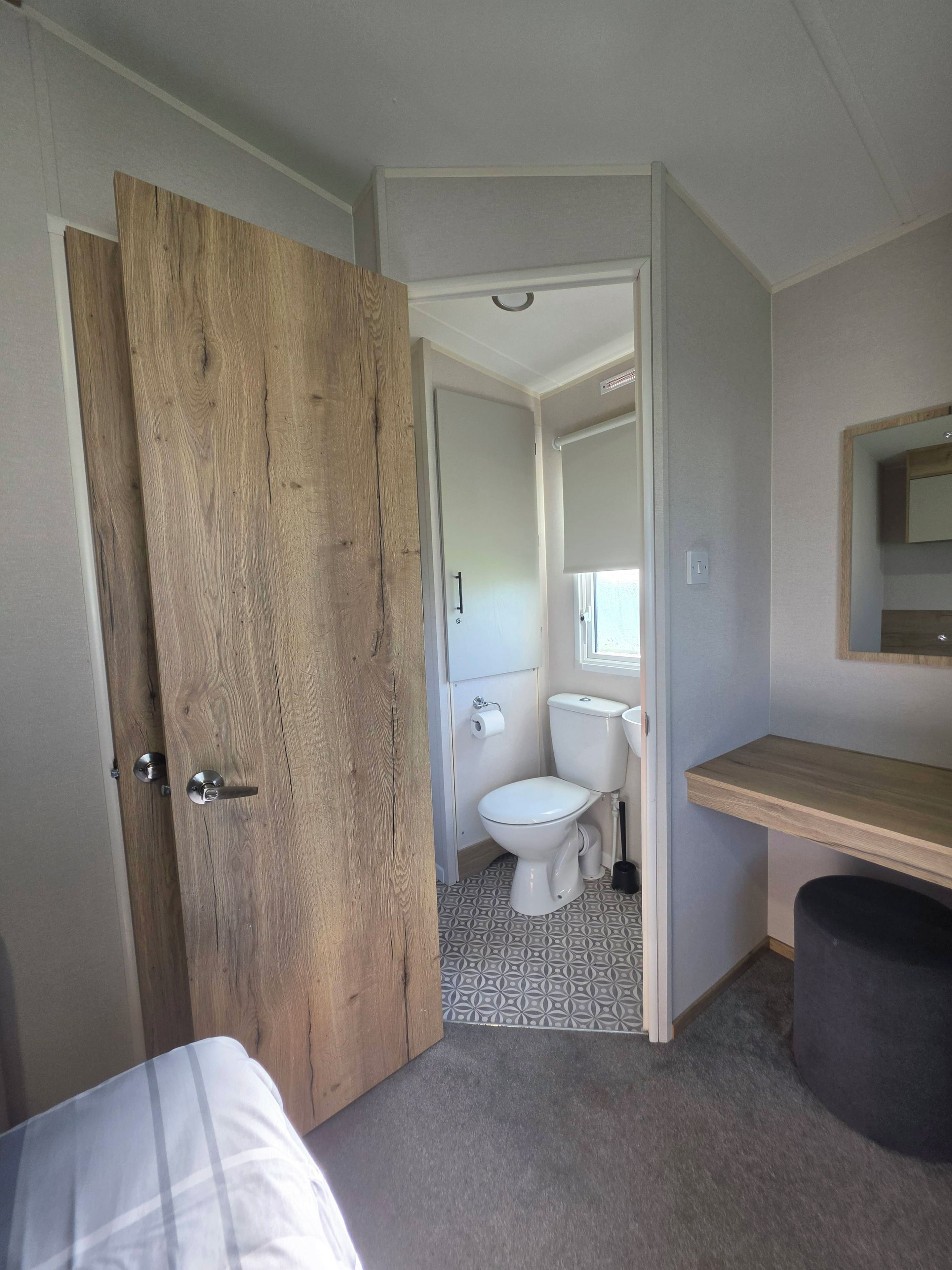 A bathroom with a toilet, a wooden door, a mirror, and a small shelf.