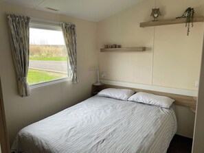 Ein Schlafzimmer mit Bett, Vorhängen, einem Nachttisch, einer Lampe, einem Regal mit einem Schild und einem Fenster mit Blick ins Freie.