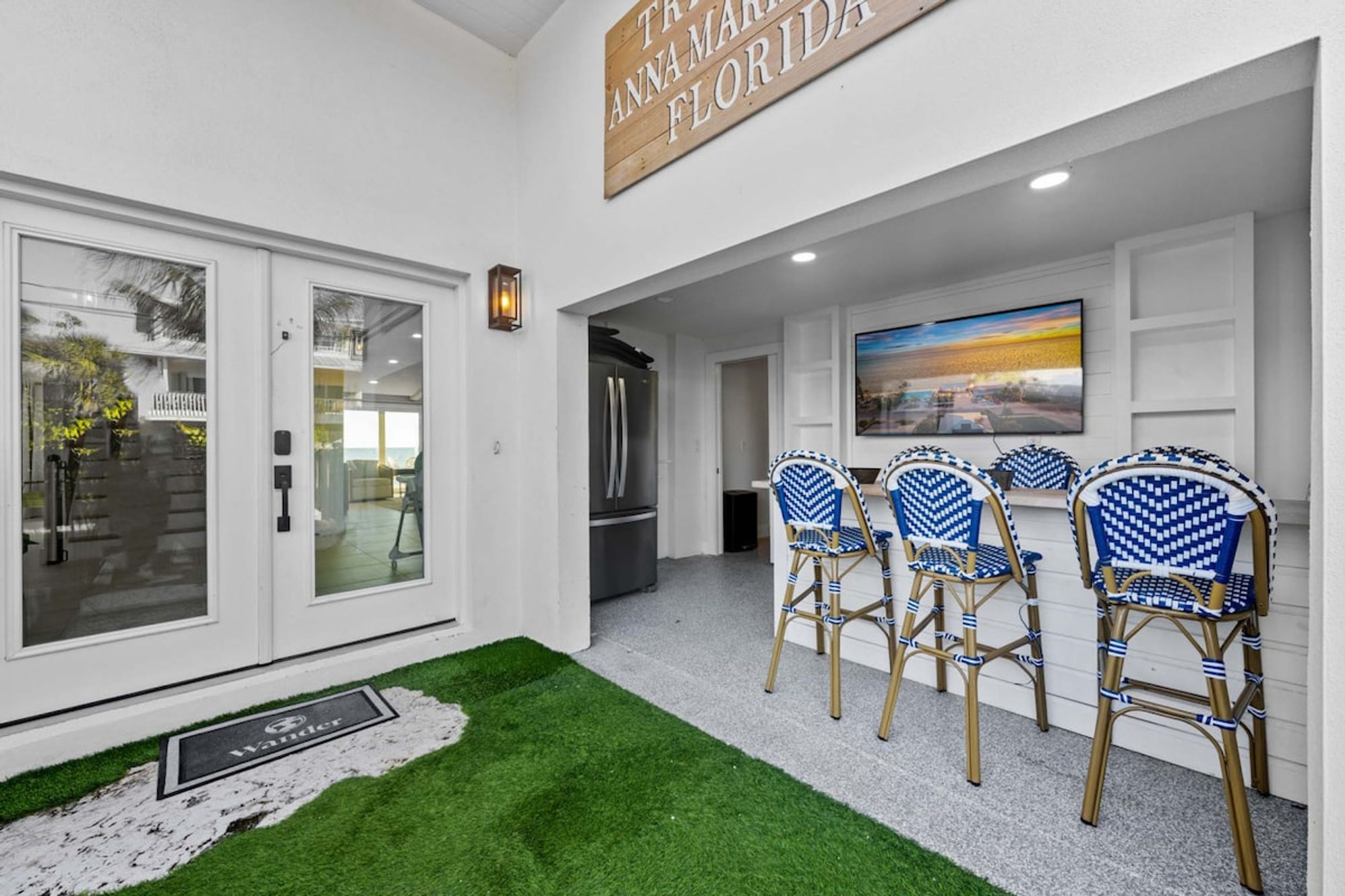 A modern interior with a flat-screen TV, a dining area with blue and white patterned chairs, and a sign reading 'The Anna Maria Florida'.