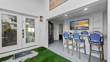 A modern interior with a flat-screen TV, a dining area with blue and white patterned chairs, and a sign reading 'The Anna Maria Florida'.
