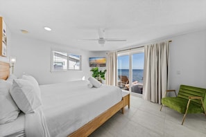 Ein Hotelzimmer mit einem Bett, einem Sessel, einem Fenster mit Meerblick und einem Deckenventilator.