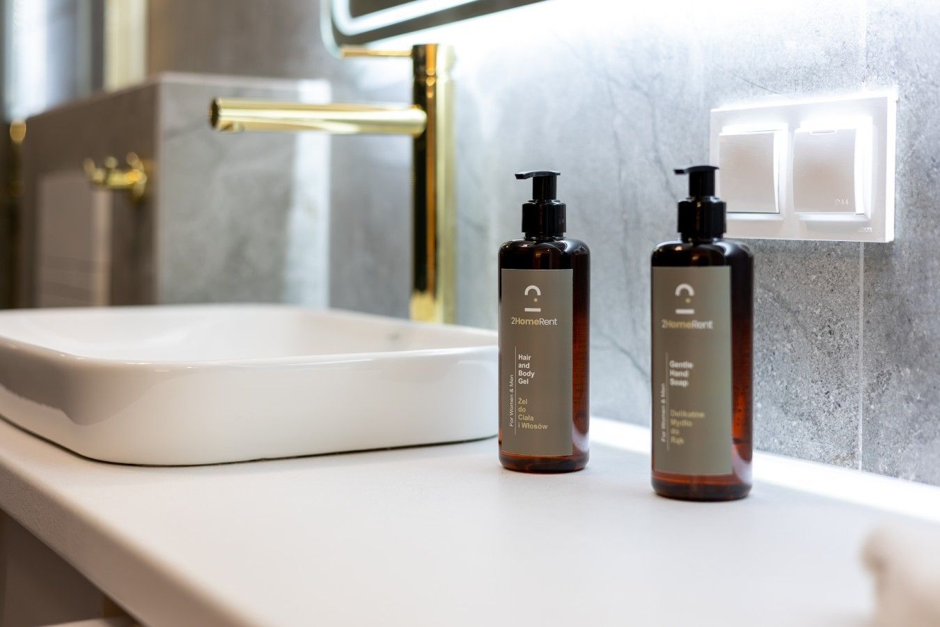 Een badkamer met een witte wasbak, twee flessen haar- en bodygel, en een gouden kraan.
