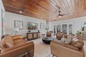 A spacious living area with leather sofas, a coffee table, and a fireplace. There are framed pictures on the walls and a ceiling fan. - Fantasea -beachfront - Heated Pool -golf Cart - Volleyball Court (Anna Maria)