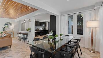 Una cocina moderna con armarios oscuros, una isla central y un comedor con mesa de vidrio y sillas negras.