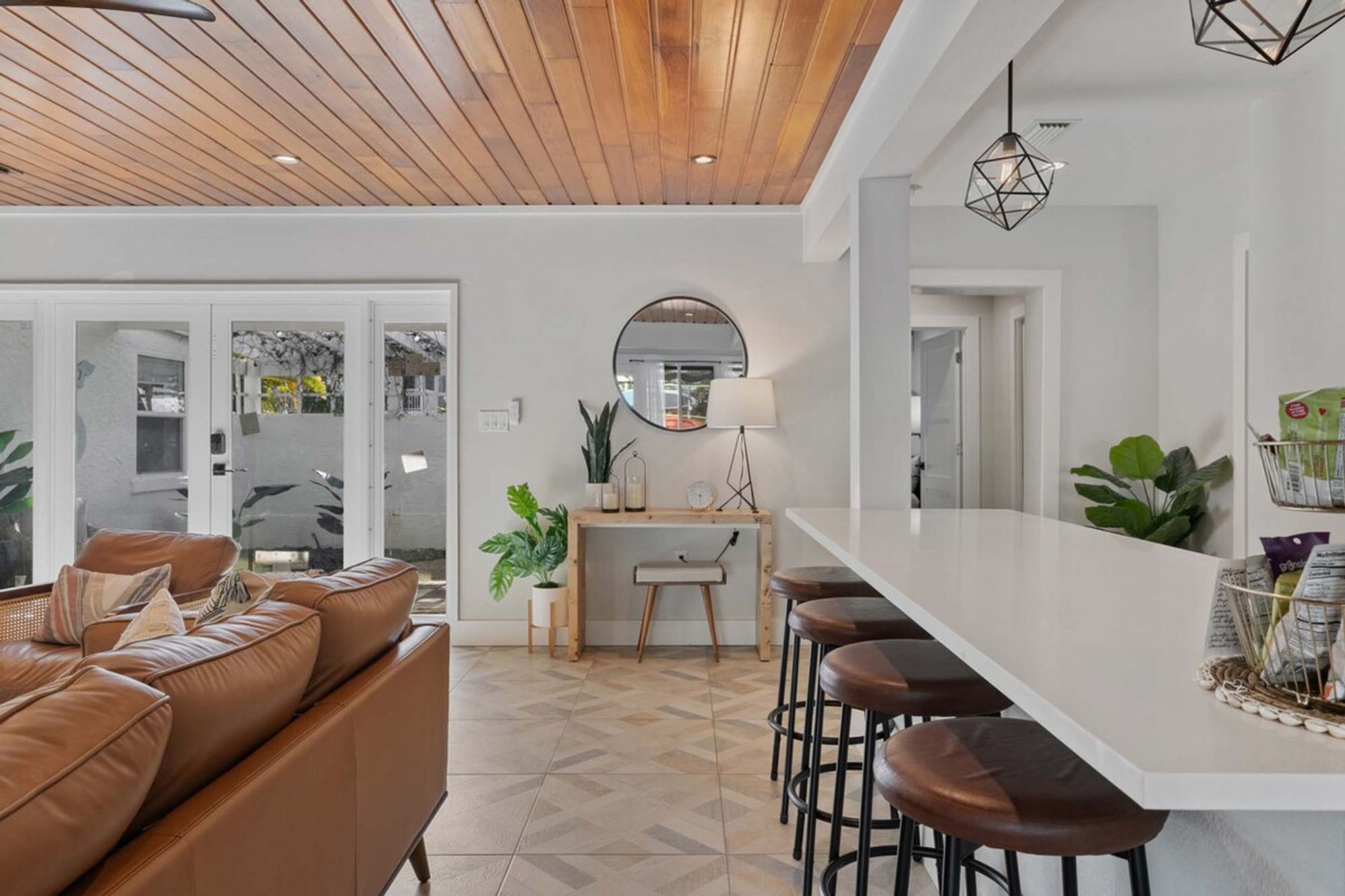A modern kitchen with a white countertop, bar stools, and a wooden ceiling.