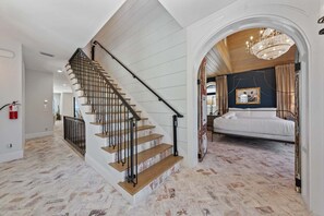 A staircase with a wooden finish and black handrails leading to a bedroom with a bed and a chandelier. - Serendipity Deux -luxury Beachfront Pool Spa - Golf Cart -elevator (Anna Maria)