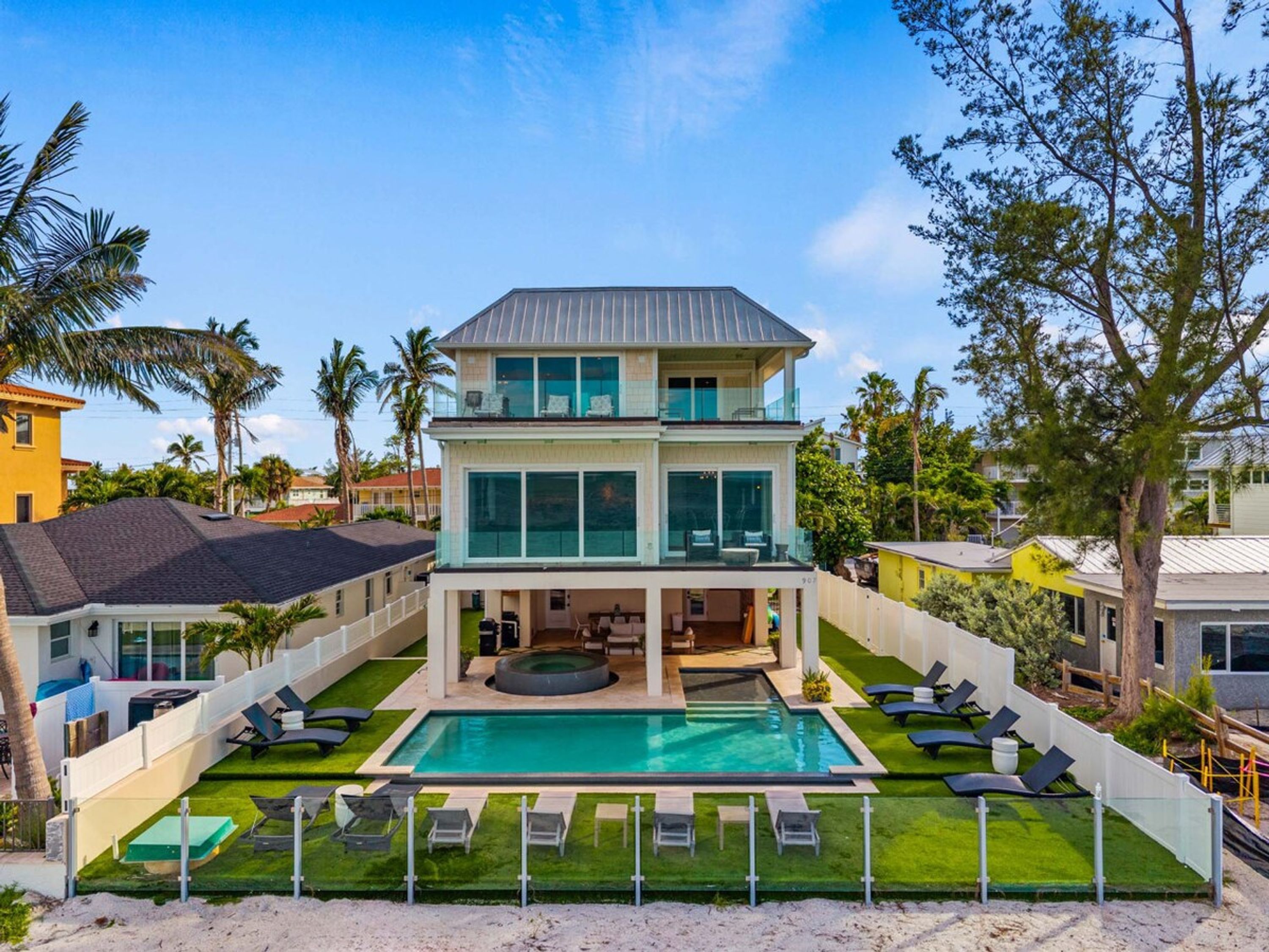 A two-story house with a swimming pool, multiple lounge chairs, and a fenced backyard.