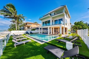 A modern two-story house with a swimming pool, multiple lounge chairs, and a well-maintained lawn. - Cloud 9 -beachfront Pool Spa -bean Point- Golf Cart (Anna Maria)