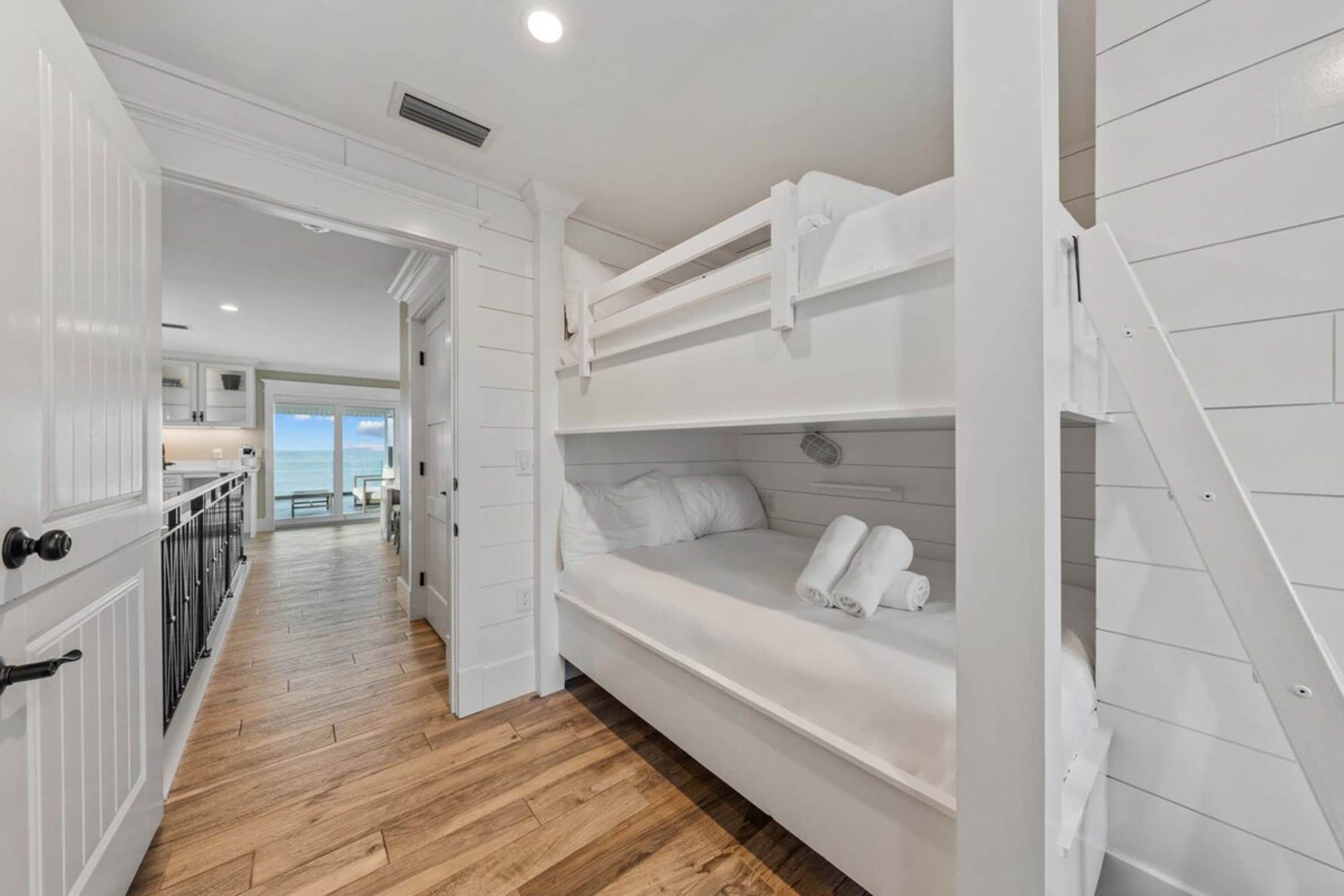 A room with a bunk bed, wooden flooring, and a view to the outside.