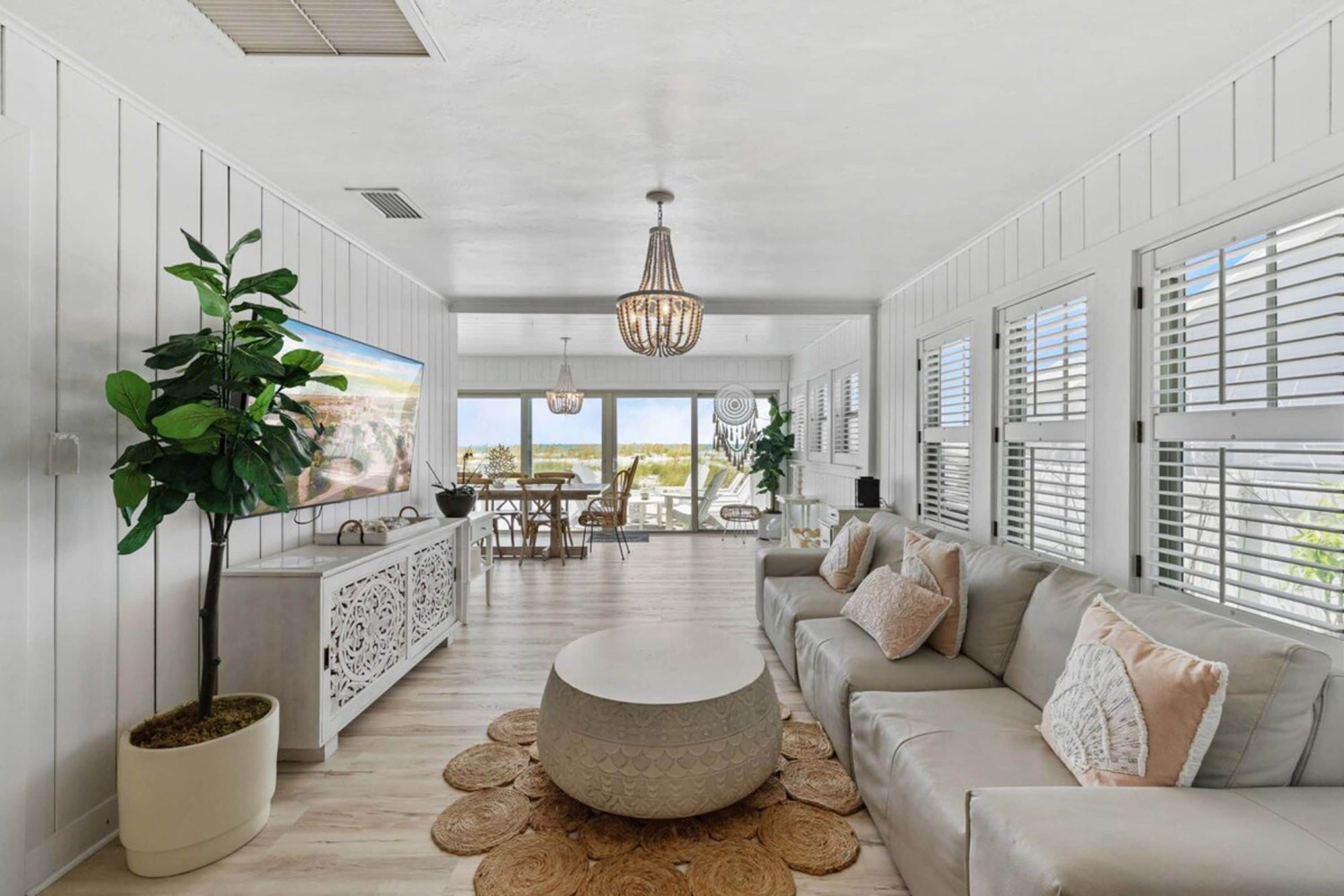 A spacious living area with a large sofa, a dining table, and a television mounted on the wall.