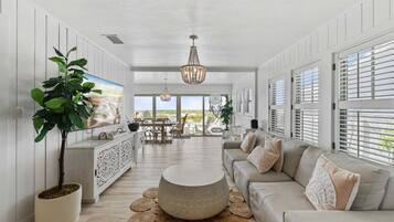 A spacious living area with a large sofa, a dining table, and a television mounted on the wall.