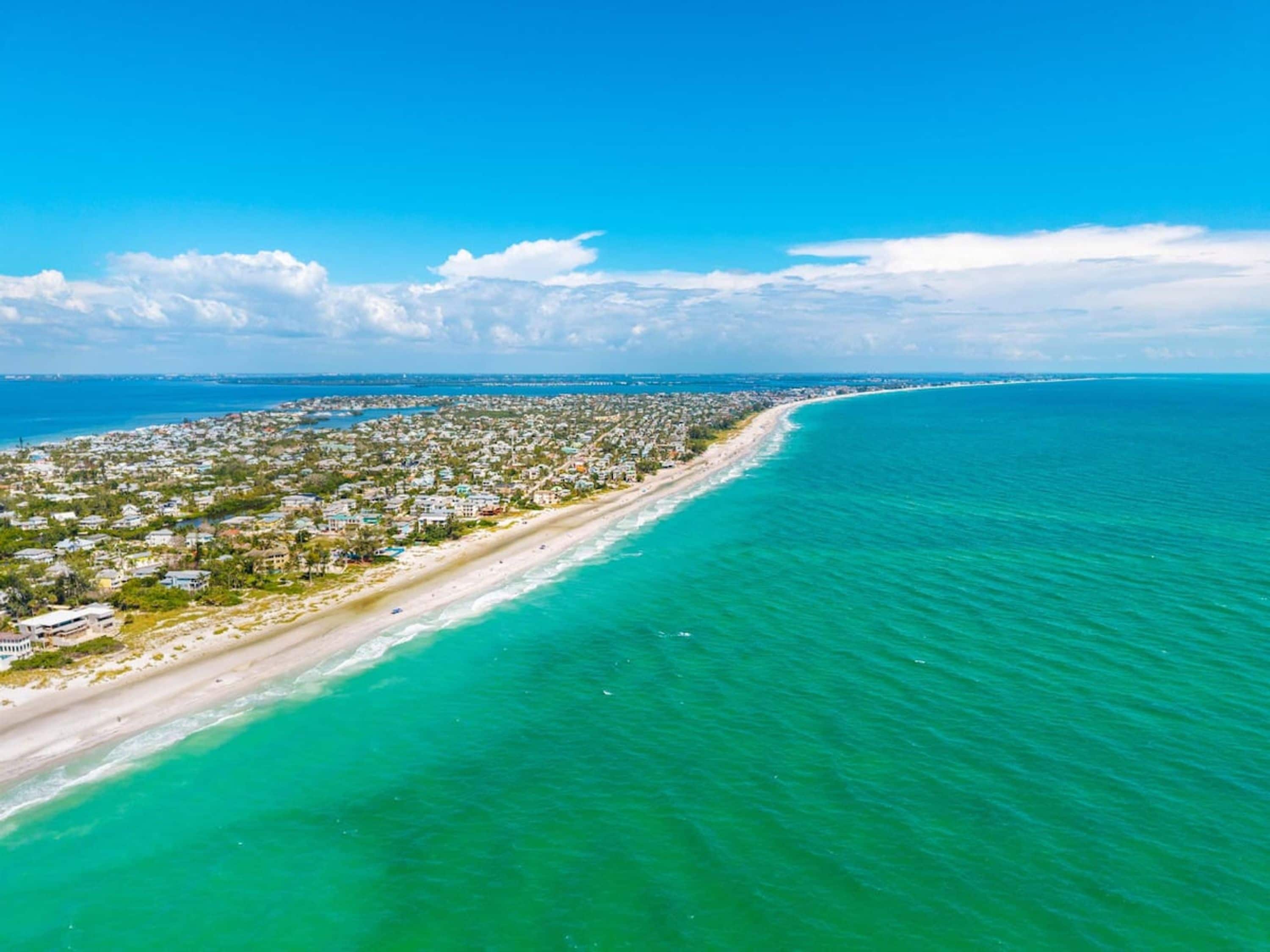 An aerial view of a coastal area with a long stretch of beach and a densely populated residential area.