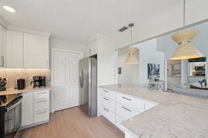 A modern kitchen with white cabinetry, a stainless steel refrigerator, and a marble countertop. - Salt Sol - Heated Pool -canal-front -golf Cart -dock (Anna Maria)