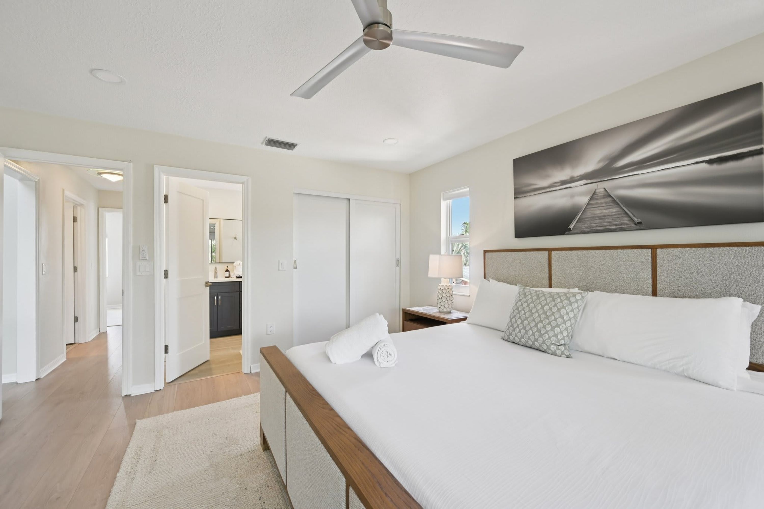 A bedroom with a bed, a ceiling fan, a painting, and a view of a dock.