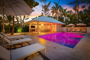 A pool area with lounge chairs, a covered seating area, and a pool with a gradient lighting effect. - Limefish Luxury - Gulf Front Pool -sunset Views -beach Access (Holmes Beach)