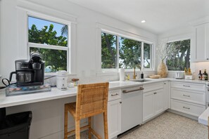 A modern kitchen with white cabinetry, a coffee maker, a toaster, and a wicker chair. - Limefish Luxury - Gulf Front Pool -sunset Views -beach Access (Holmes Beach)