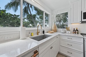 A modern kitchen with a large window, white cabinetry, and a countertop with various items. - Limefish Luxury - Gulf Front Pool -sunset Views -beach Access (Holmes Beach)