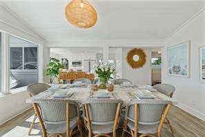 A dining area with a large table set for six, surrounded by wicker chairs, with a hanging light fixture above. - Limefish Luxury - Gulf Front Pool -sunset Views -beach Access (Holmes Beach)