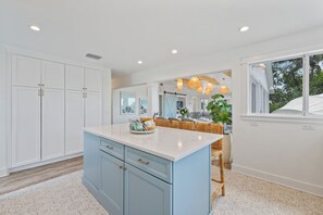 A modern kitchen with white cabinets, a blue island, and a dining area with wicker furniture. - Limefish Luxury - Gulf Front Pool -sunset Views -beach Access (Holmes Beach)