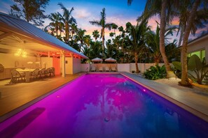 A swimming pool with a sunset view, surrounded by palm trees and a covered outdoor seating area. - Limefish Luxury - Gulf Front Pool -sunset Views -beach Access (Holmes Beach)