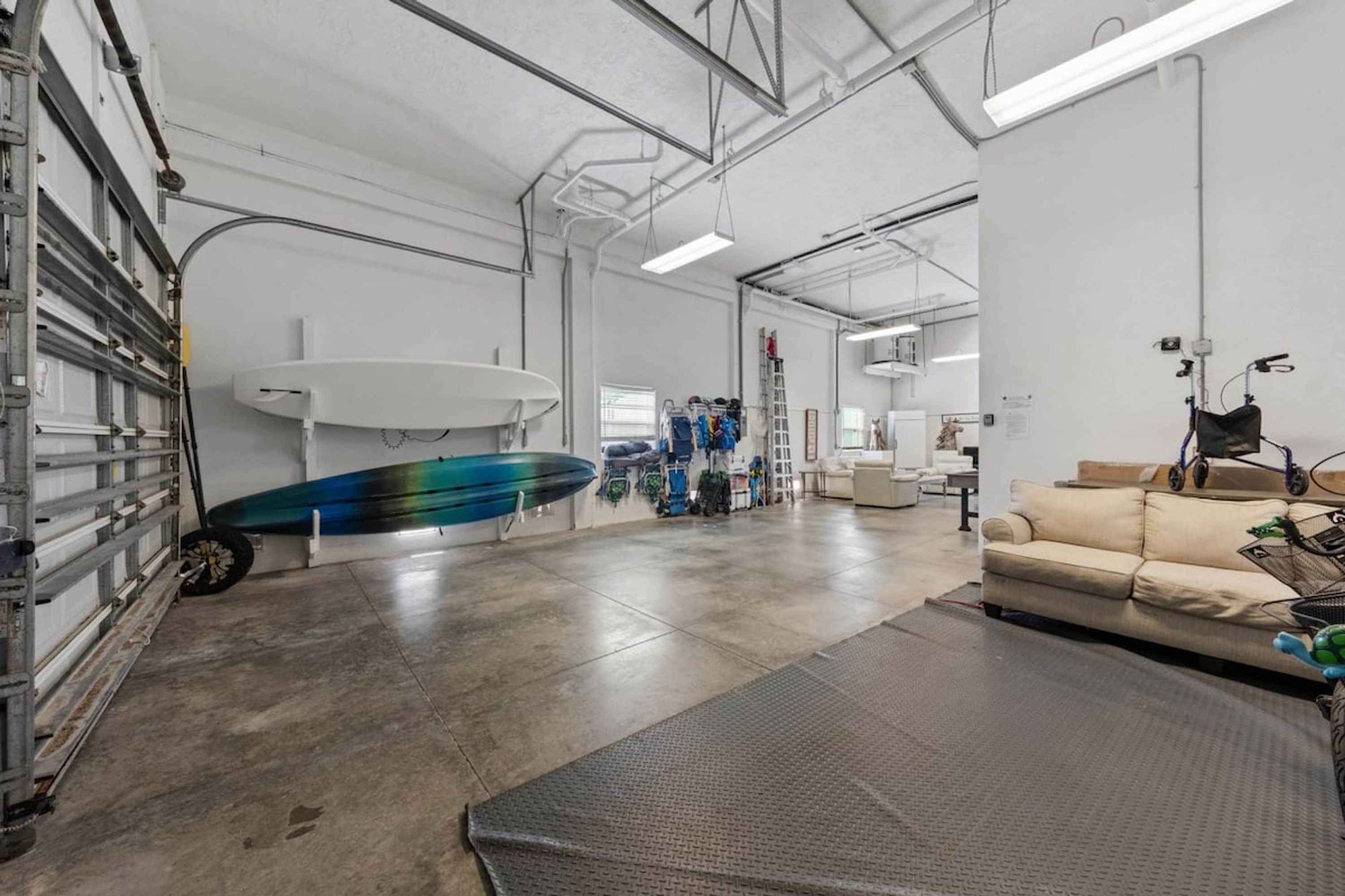 A spacious indoor area with a concrete floor, a surfboard leaning against a wall, and a couch in the foreground.