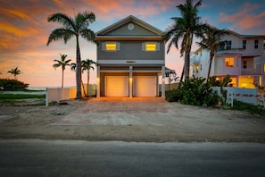 A two-story house with a garage, surrounded by palm trees, at sunset. - Serendipity -beachfront -hot Tub -golf Cart -elevator (Anna Maria)