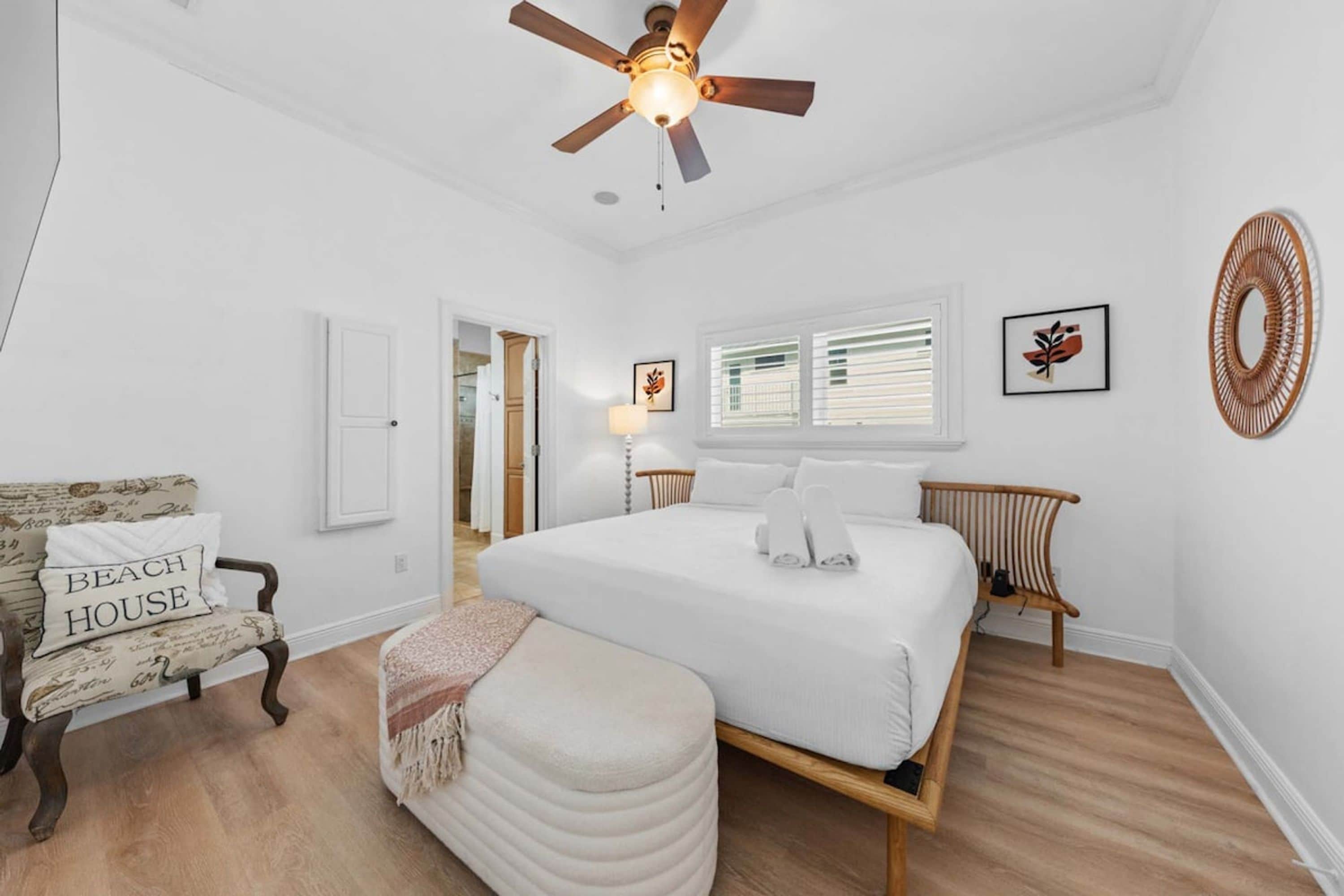 A bedroom with a large bed, a ceiling fan, a chair, and a bedside table.