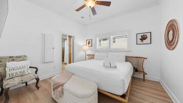 A bedroom with a large bed, a ceiling fan, a chair, and a bedside table.