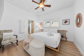 Un dormitorio con una cama grande, un ventilador de techo, una silla y una mesita de noche.