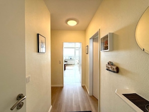 A hallway with a door on the left, a light fixture on the ceiling, and a view into a kitchen area. - Uthlande Holiday Apartment 14 (Wyk auf Foehr)