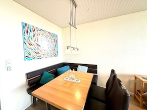 A modern dining area with a wooden table, black cushioned seating, and a colorful abstract painting on the wall. - Uthlande Holiday Apartment 14 (Wyk auf Foehr)