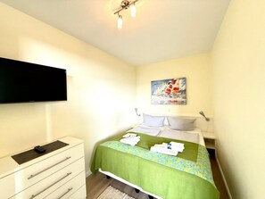 A hotel room with a bed, a flat-screen TV, a dresser, and a painting on the wall. - Uthlande Holiday Apartment 14 (Wyk auf Foehr)