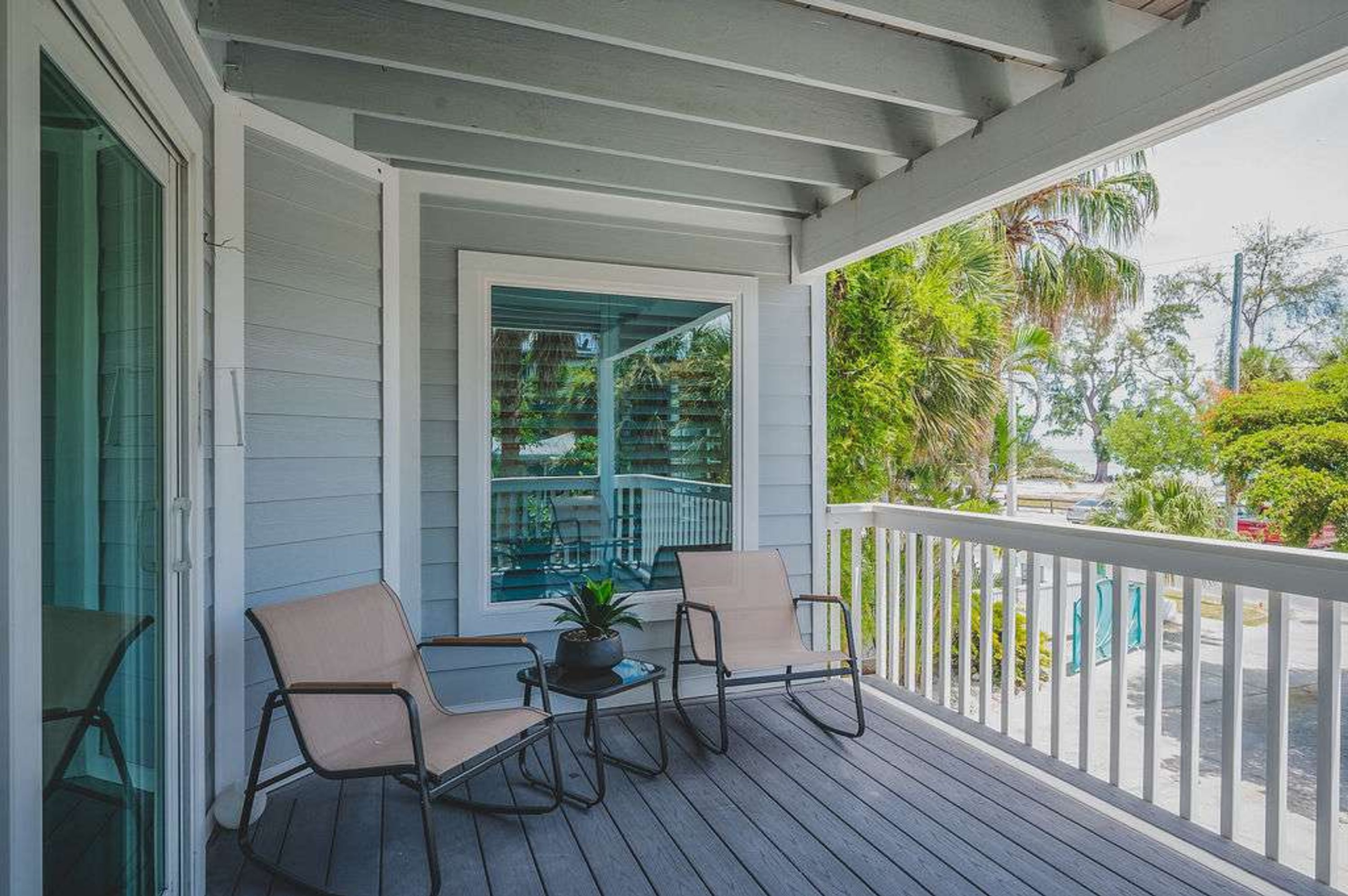 A covered porch with two chairs and a small table, overlooking a pool and lush greenery.