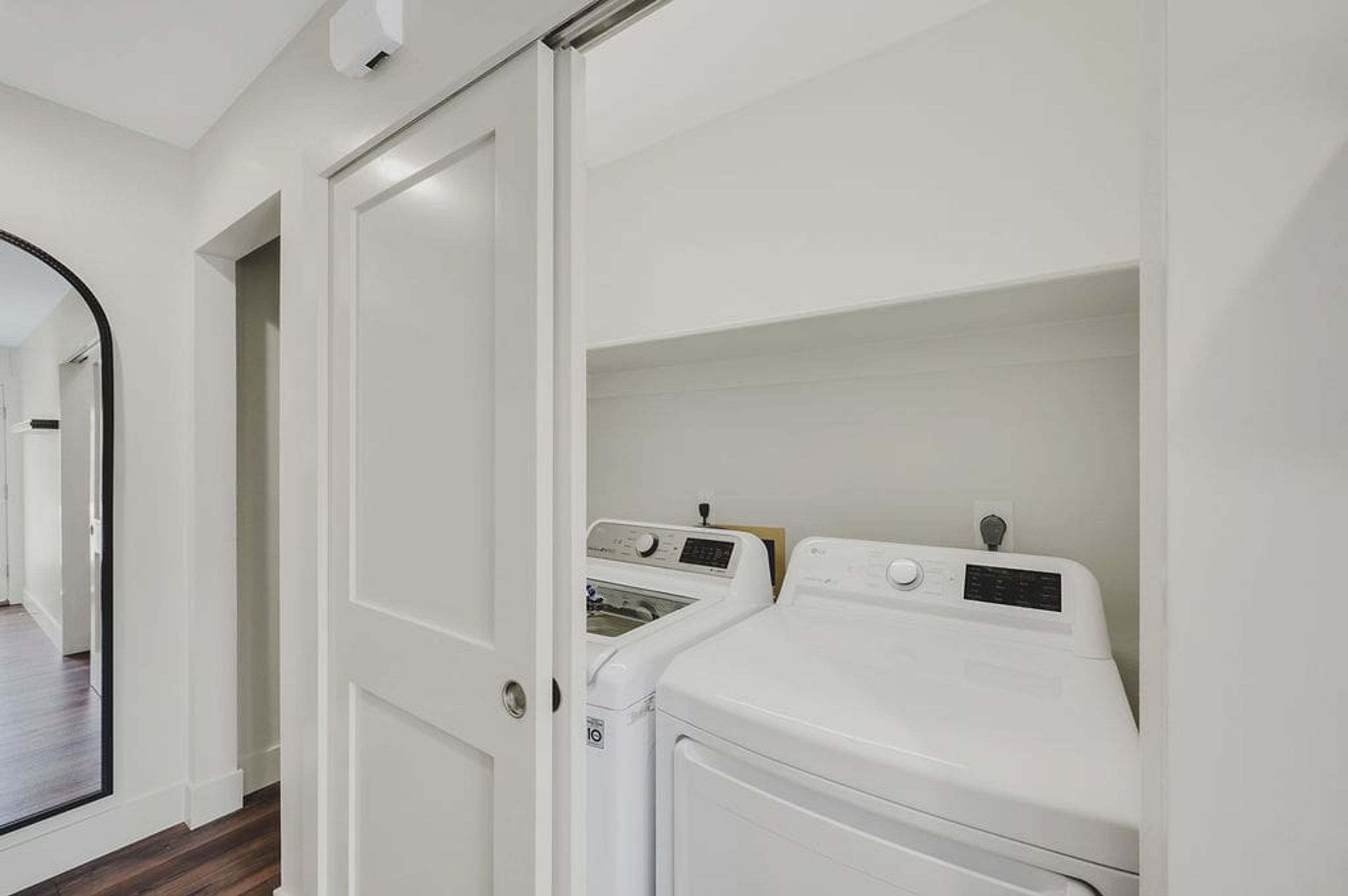 A laundry room with two white washing machines and a door leading to another room.