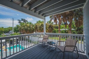 A covered outdoor area with a pool, two chairs, and a view of palm trees and a road. - Sandcastle -steps to Beach -pool - Golf Cart (Anna Maria)