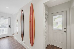 A hallway with two surfboards mounted on the wall, a white door, and a window with blinds. - Sandcastle -steps to Beach -pool - Golf Cart (Anna Maria)