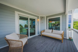 A covered porch with a wooden bench and wicker chairs, glass doors leading to a backyard, and a hanging light fixture.