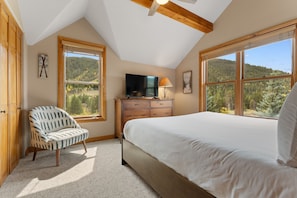 A bedroom with a bed, a dresser, a television, and two windows with a view of a forested landscape. - Hr5959-2 (Keystone)