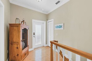 A hallway with a wooden cabinet, a white door, and a sign on the wall. - Beach Escape Heated Pool Walk to Beach Golf Cart (Holmes Beach)