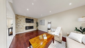 A modern living room with a stone wall, a flat-screen TV, a fireplace, a sofa, and a coffee table. - Brampton Gem - Spacious 4BR & Parking (Brampton)