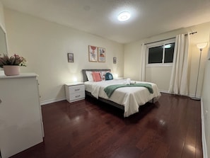 A bedroom with a bed, bedside table, nightstand, potted plant, artwork, and a window with curtains. - Brampton Gem - Spacious 4BR & Parking (Brampton)