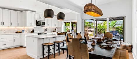 Una cocina moderna con armarios blancos, una isla central y un comedor con una mesa grande y sillas.