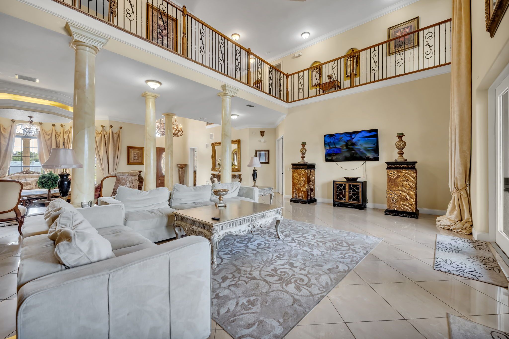 A spacious living room with a high ceiling, a grand staircase, and a television mounted on the wall.