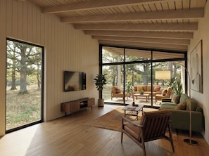 Ein modernes Wohnzimmer mit großem Fernseher, Holzboden und Blick auf einen Garten durch große Fenster.