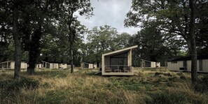 Eine moderne, minimalistische Holzhütte mit einem großen Panoramafenster, umgeben von hohen Bäumen und einer grünen Landschaft.